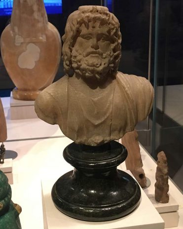 Der Gott Serapis, der sich aus den ägyptischen Göttern AOsiris, Apis und Amun zusammensetzt. Auch die Attribute der griechischen Götter Zeus und Asclepius vereinen sich in ihm Reichmuseum von Leiden, Niederlande